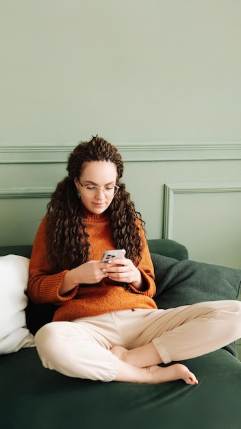 Szczęśliwa kobieta relaksująca się na kanapie przy użyciu telefonu komórkowego do zakupów i mediów społecznościowych w domu e-commerce i