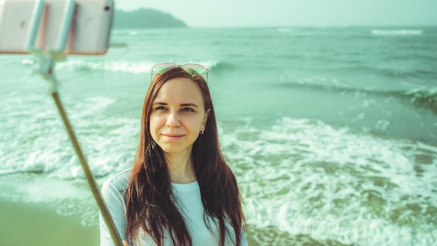 Szczęśliwa kobieta robiąca selfie w pobliżu morza Z góry zadowolona kobieta używa monopodu ze smartfonem do robienia selfie w pobliżu falującego morza na plaży