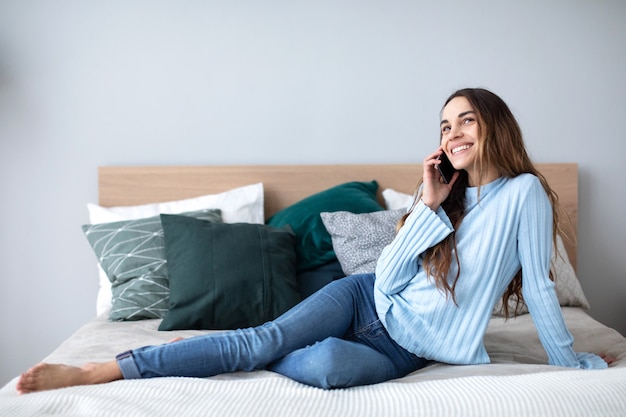 Zdjęcie szczęśliwa kobieta rozmawia na smartfonie w domu na kanapie. koncepcja ludzi, technologii i komunikacji.