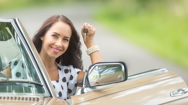 Szczęśliwa kobieta siada do kabrioletu z kluczykiem w dłoni, korzystając z wypożyczalni samochodów.