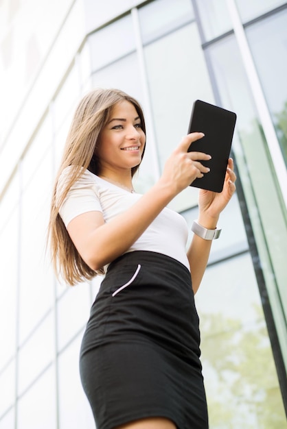 Szczęśliwa kobieta stojąc na ulicy przed budynkiem biurowym i za pomocą komputera typu Tablet.