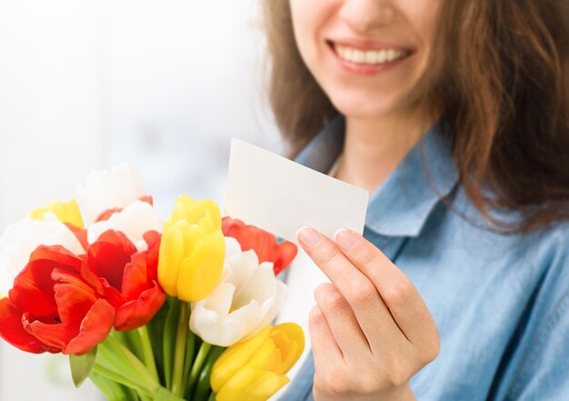 Szczęśliwa kobieta trzyma bukiet tulipanów w dłoniach i czyta notatkę