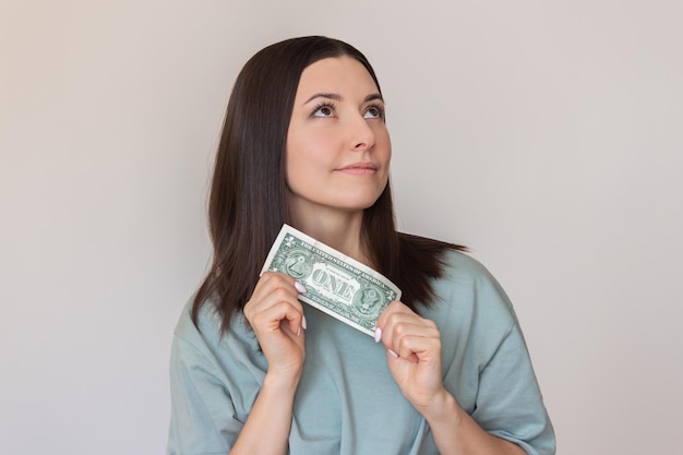 Zdjęcie szczęśliwa kobieta trzyma dolara w dłoniach i myśli, jak wydawać pieniądze koncepcja finansów