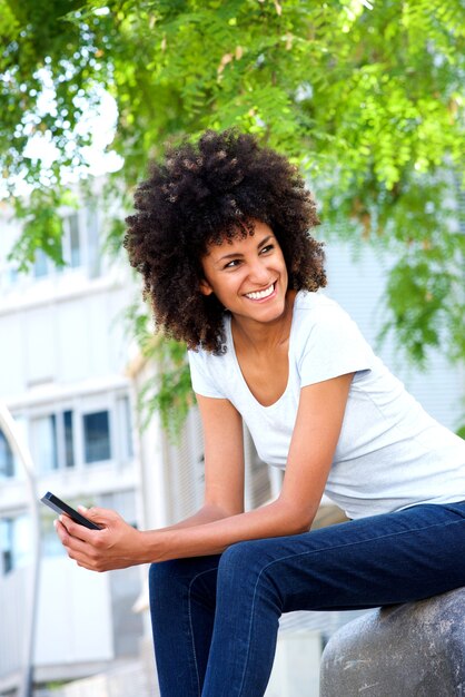 Szczęśliwa kobieta trzyma mądrze telefon outside w parku