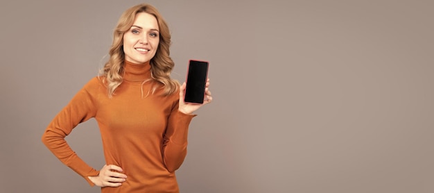Szczęśliwa kobieta trzyma nowoczesny inteligentny telefon szare tło urządzenie mobilne Portret kobiety na białym tle baner nagłówka z miejscem na kopię