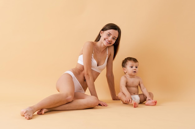 Szczęśliwa kobieta trzyma swoje dziecko na kolorowym tle - młoda kobieta ubrana w bieliznę opiekująca się swoim małym synkiem - koncepcja ciąży, macierzyństwa, ludzi i oczekiwania