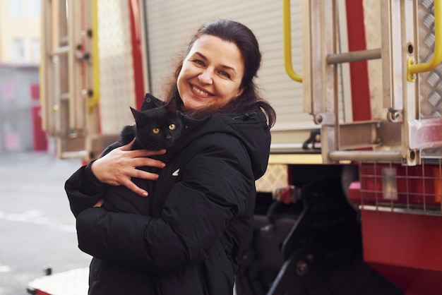 Szczęśliwa kobieta trzyma swojego czarnego kota w rękach ner wóz strażacki na zewnątrz