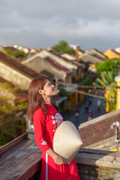 Szczęśliwa kobieta ubrana w wietnamską sukienkę Ao Dai podróżnik zwiedzający widok na dachu w Hoi Starożytne miasto w Wietnamie punkt orientacyjny i popularne wśród atrakcji turystycznych Wietnam i koncepcja podróży na południowy wschód