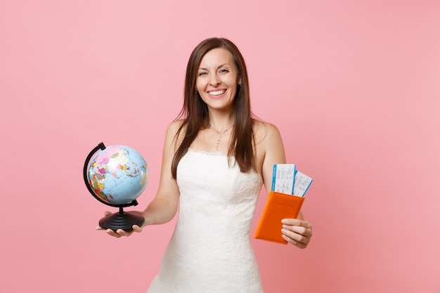 Szczęśliwa kobieta w białej sukni trzymająca światową kulę ziemską, paszport, bilet na pokład, wyjazd za granicę, wakacje