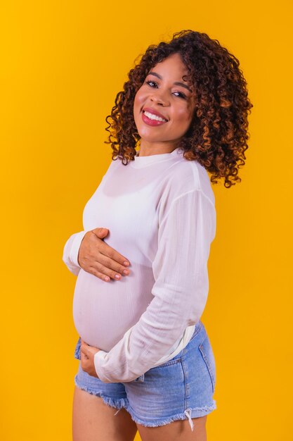 Szczęśliwa kobieta w ciąży afro dotykając jej brzucha. Portret w ciąży młoda matka, pieszcząc jej brzuch i uśmiechając się z bliska. koncepcja zdrowej ciąży. Pionowy