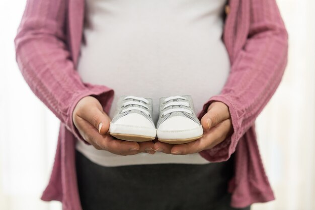 Zdjęcie szczęśliwa kobieta w ciąży trzyma dziecięce buciki