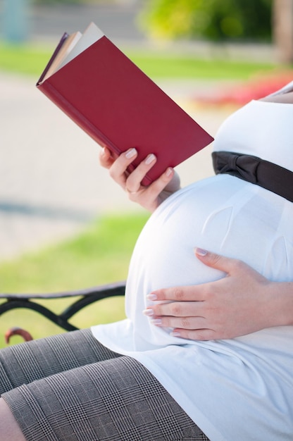 Szczęśliwa kobieta w ciąży z książką w parku na świeżym powietrzu