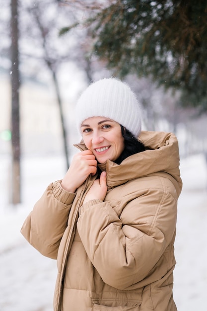 Szczęśliwa kobieta w kapeluszu grzeje się w płaszczu Stoi w mieście zimą pod śniegiem