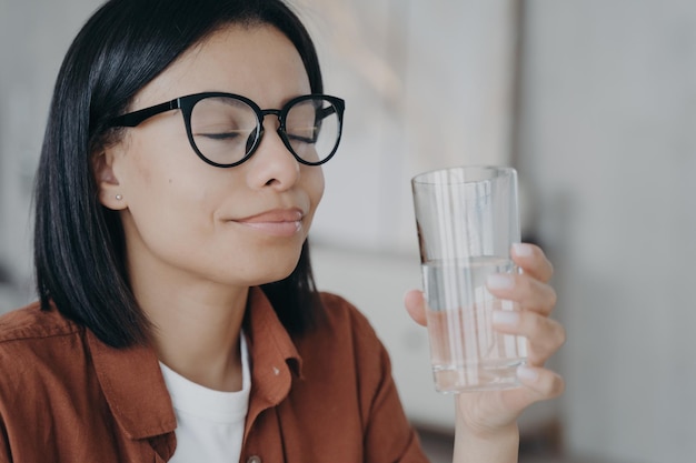 Szczęśliwa kobieta w okularach trzyma szklankę czystej wody zamknięte oczy Zdrowy styl życia wellness