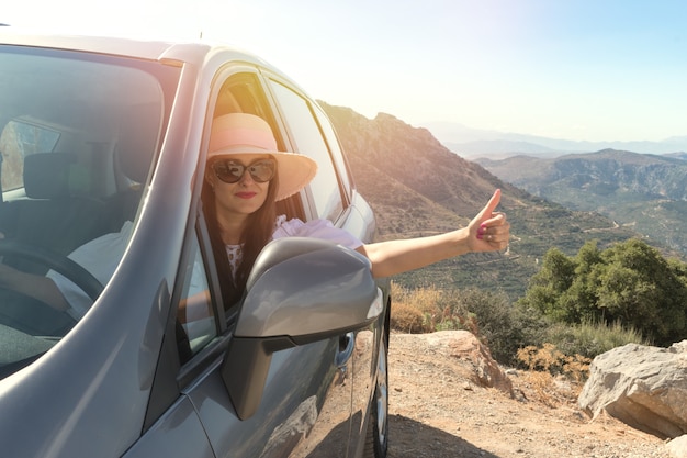 Szczęśliwa kobieta w samochodzie jadąca ulicą i wskazująca kciukiem w górę