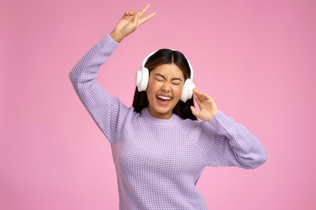 Szczęśliwa kobieta w słuchawkach słuchająca muzyki na różowym tle