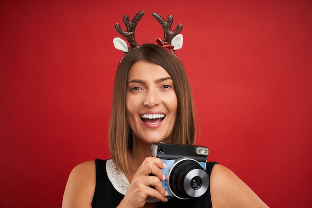 szczęśliwa kobieta w świątecznym nastroju robi błyskawiczne zdjęcia na czerwonym tle
