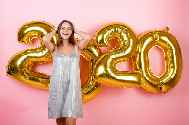 Szczęśliwa kobieta w wakacyjnej sukni z nowego roku 2020 balonami odizolowywającymi nad menchiami