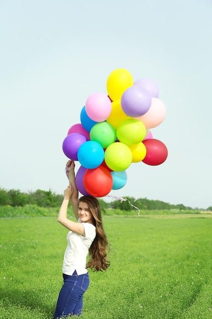 Szczęśliwa kobieta z kolorowymi balonami w polu na niebieskim niebie