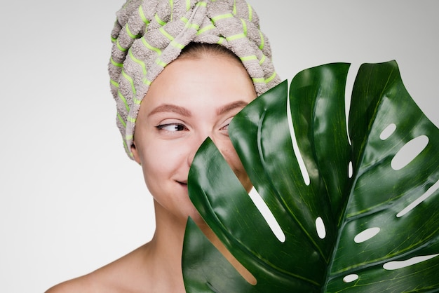 Szczęśliwa kobieta z ręcznikiem na głowie po prysznicu trzyma zielony liść