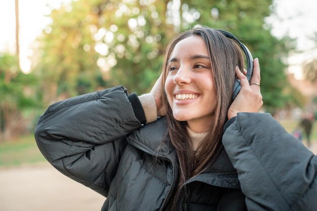 Szczęśliwa kobieta z słuchawkami ciesząca się muzyką podcast nasze audiobooki na świeżym powietrzu w parku