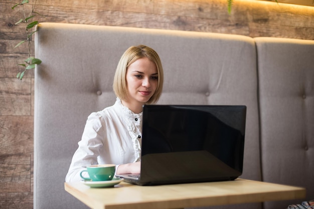 Szczęśliwa kobieta za pomocą laptopa w kawiarni Młoda piękna dziewczyna siedzi w kawiarni i pracuje na komputerze