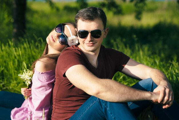 Szczęśliwa kochająca młoda para spędzająca czas w parku, siedząca na zielonym trawniku w słoneczny letni dzień