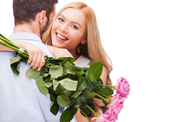 Szczęśliwa kochająca para. Piękna młoda kochająca para przytula się, podczas gdy kobieta trzyma bukiet różowych róż i uśmiecha się i oboje stoją na białym tle
