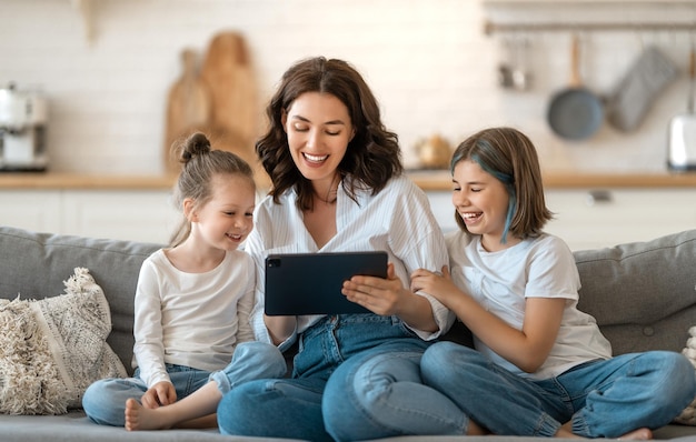 Szczęśliwa kochająca rodzina. Młode dziewczyny matki i córki przy użyciu komputera typu tablet do zdalnej rozmowy z przyjaciółmi. Zabawna mama i kochane dzieci bawią się przebywając w domu.