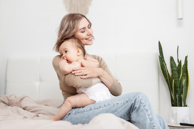 Szczęśliwa kochająca rodzina Troskliwa matka przytula swoją córeczkę siedząc na łóżku w sypialni