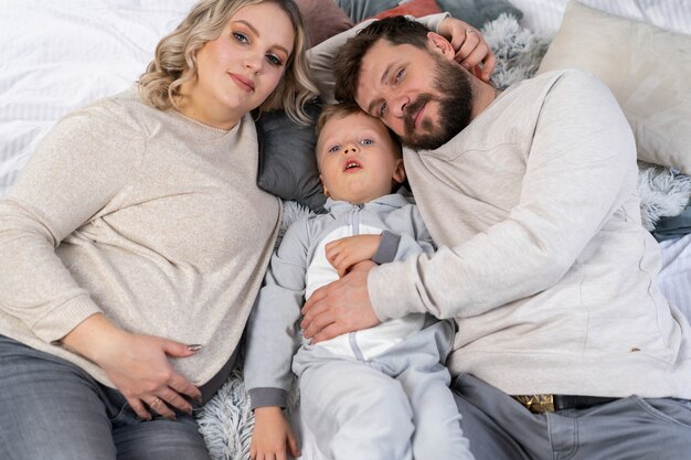 Szczęśliwa koncepcja rodziny Matka tata i synek bawią się w domu Kaukaska rodzina w domu Mama w ciąży broda tata i zabawny mały chłopiec leżą na kanapie
