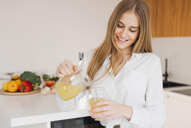 Szczęśliwa ładna blondynka pije sok pomarańczowy w kuchni.