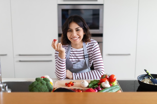 Szczęśliwa ładna latynoska kobieta gotuje w domu, pokazując organicznie pomidora