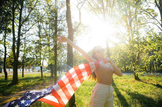 Szczęśliwa ładna młoda kobieta trzyma flagę Patriotyczne święto i obchody dnia niepodległości USA 4th