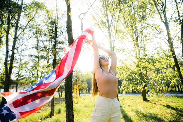 Szczęśliwa ładna młoda kobieta trzyma flagę Patriotyczne święto i obchody dnia niepodległości USA 4th