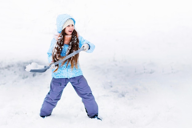 Szczęśliwa mała dziewczynka bawi się i rzuca śnieg łopatą