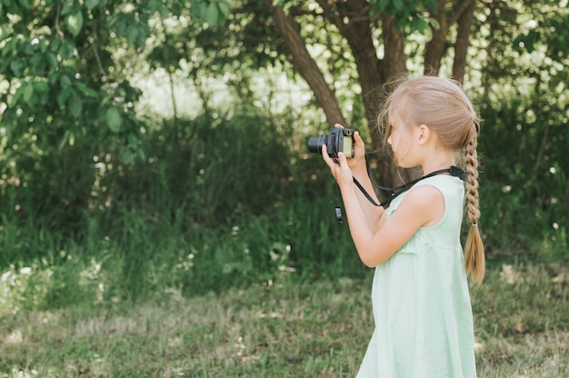 Szczęśliwa mała dziewczynka fotografuje letni naturalny krajobraz za pomocą aparatu, korzystając z podglądu na żywo