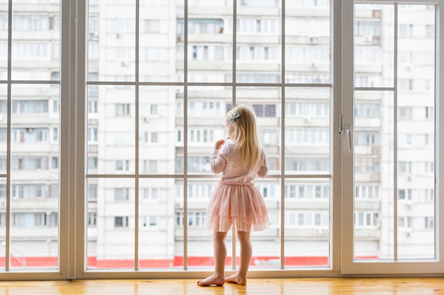 Zdjęcie szczęśliwa mała dziewczynka jest ubranym śliczną suknię patrzeje okno