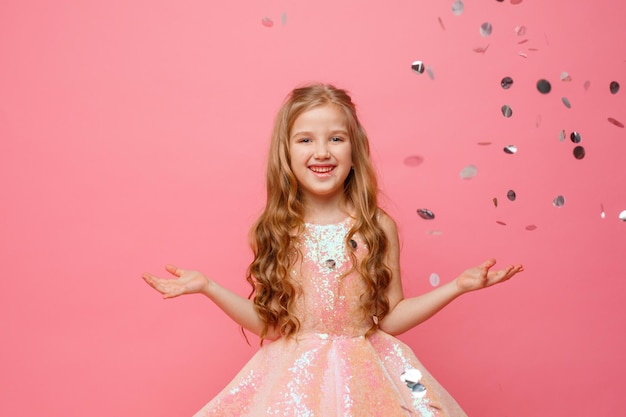 Szczęśliwa mała dziewczynka łapie konfetti na różowym tle koncepcji wakacyjnej