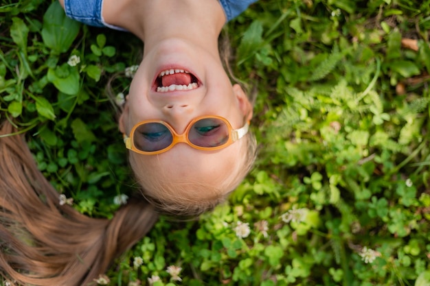 Szczęśliwa mała dziewczynka leżąca na zielonej trawie latem widok z góry Dziecko z zespołem Downa w okularach dla wzroku