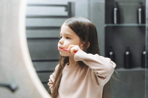 Szczęśliwa mała dziewczynka myje zęby przed lustrem w łazience Poranna higiena