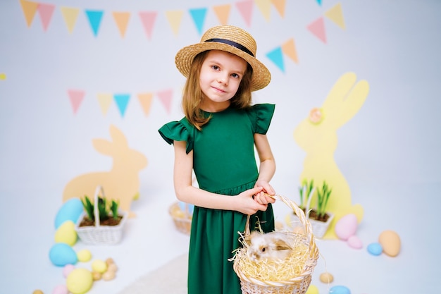 Szczęśliwa mała dziewczynka trzyma ślicznego puszystego królika z łozinowym koszem