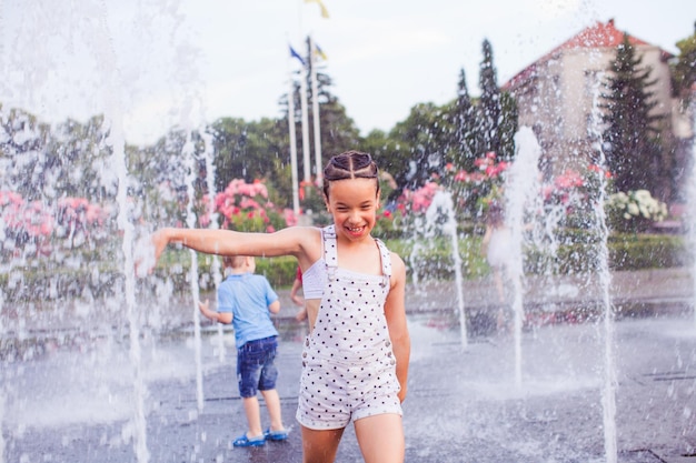 Szczęśliwa mała dziewczynka w mokrych ubraniach na środku fontanny
