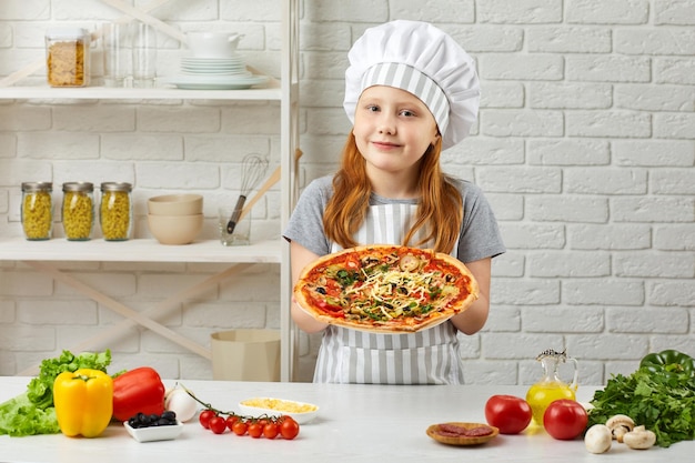 Szczęśliwa mała dziewczynka w szefa kuchni kapeluszu i fartuchu kulinarna pizza