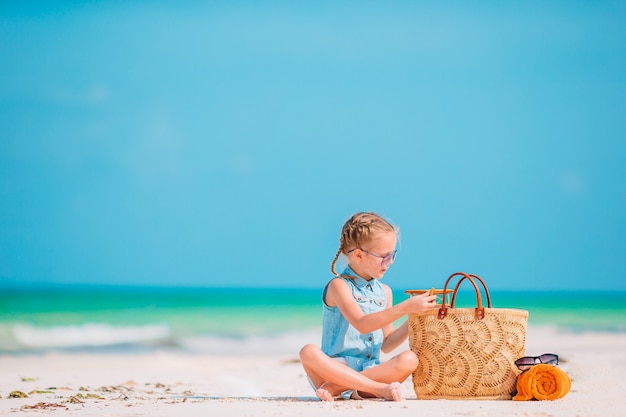 Szczęśliwa mała dziewczynka z zabawkarskim samolotem w rękach na białej piaskowatej plaży.