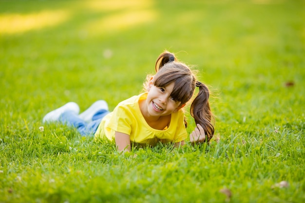Szczęśliwa mała indyjska dziewczyna w żółtej koszulce śmieje się latem na trawniku