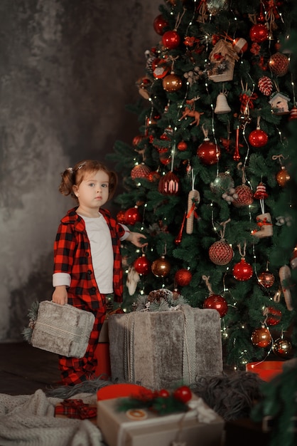 Szczęśliwa mała uśmiechnięta dziewczyna w czerwonej piżamie i Santa hat z prezentem świątecznym