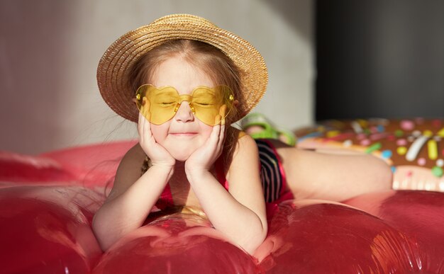 Szczęśliwa małe dziecko dziewczyna w swimsuit i słomkowym kapeluszu przygotowywa na letnią wycieczkę w domu