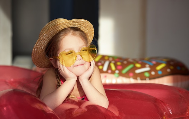 Szczęśliwa małe dziecko dziewczyna w swimsuit i słomkowym kapeluszu przygotowywa na letnią wycieczkę w domu.