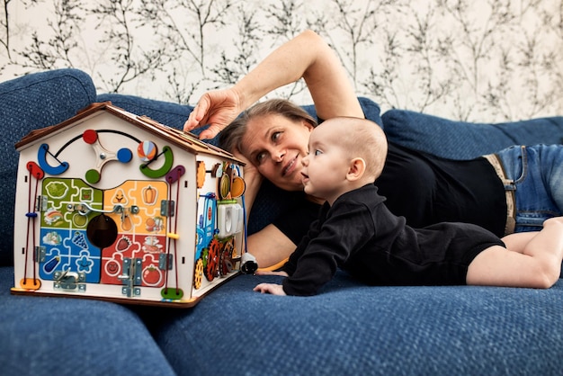 Szczęśliwa mama bawi się swoim małym dzieckiem domkiem z zabawkami, leżąc na kanapie w czarnej koszulce